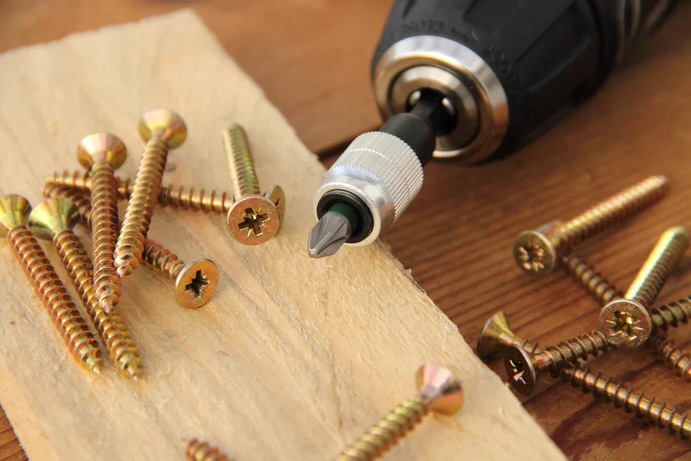 wood screws on a plank of wood near a hand drill